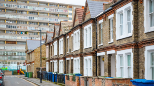 A row of traditional brick terraced houses with white windows contrasts with a large modernist apartment block in London.