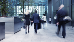 A group of professionals walking through a modern glass atrium entrance of an office building.