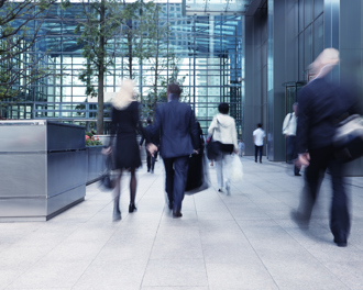 A group of professionals walking through a modern glass atrium entrance of an office building.