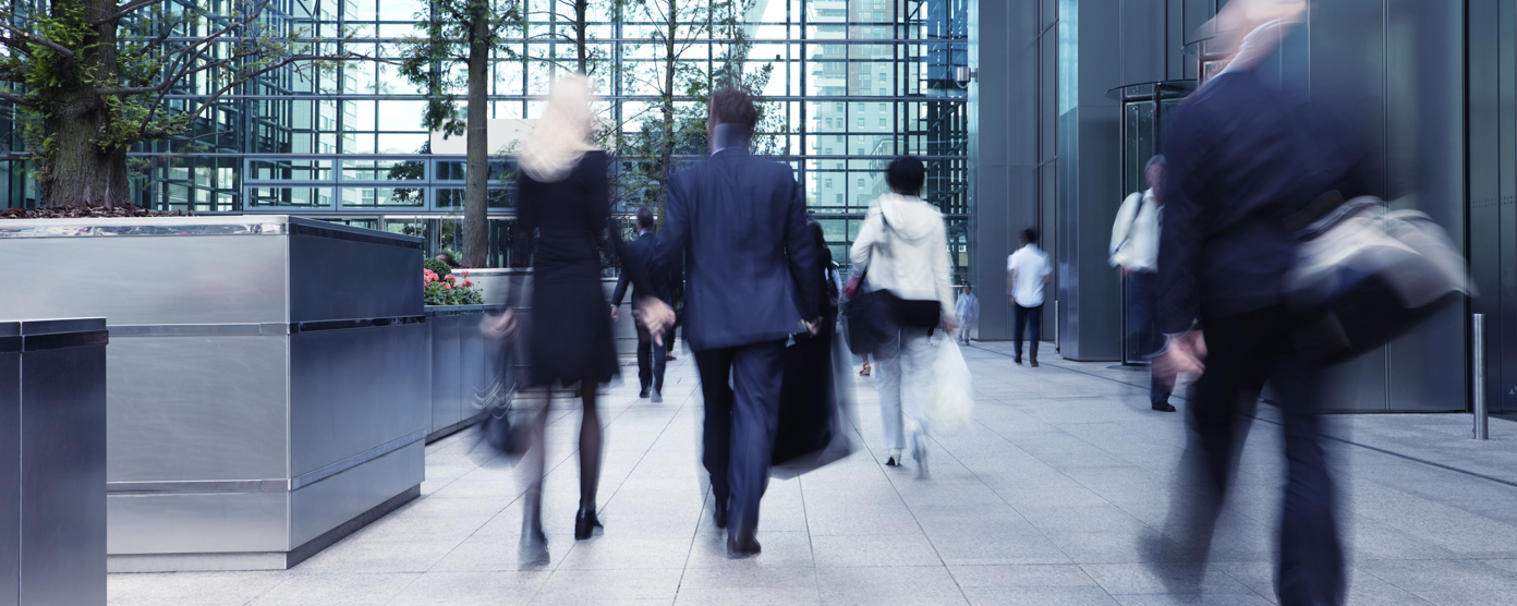 A group of professionals walking through a modern glass atrium entrance of an office building.