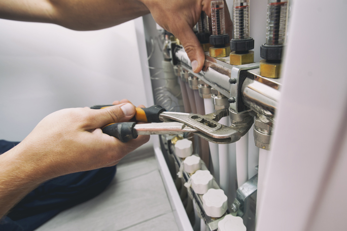  A person using a wrench to install or maintain a heating or plumbing manifold system.