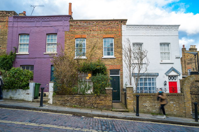 Row of colorful terraced houses on a cobbled street with a pedestrian walking by.
