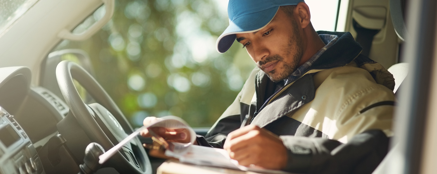 Delivery driver in a van filling out paperwork on a clipboard with parcels on the seat