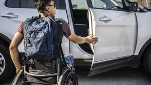Wheelchair user with a backpack opening a car door, illustrating accessible travel and independence