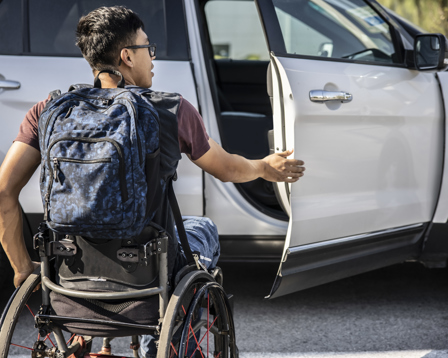 Wheelchair user with a backpack opening a car door, illustrating accessible travel and independence