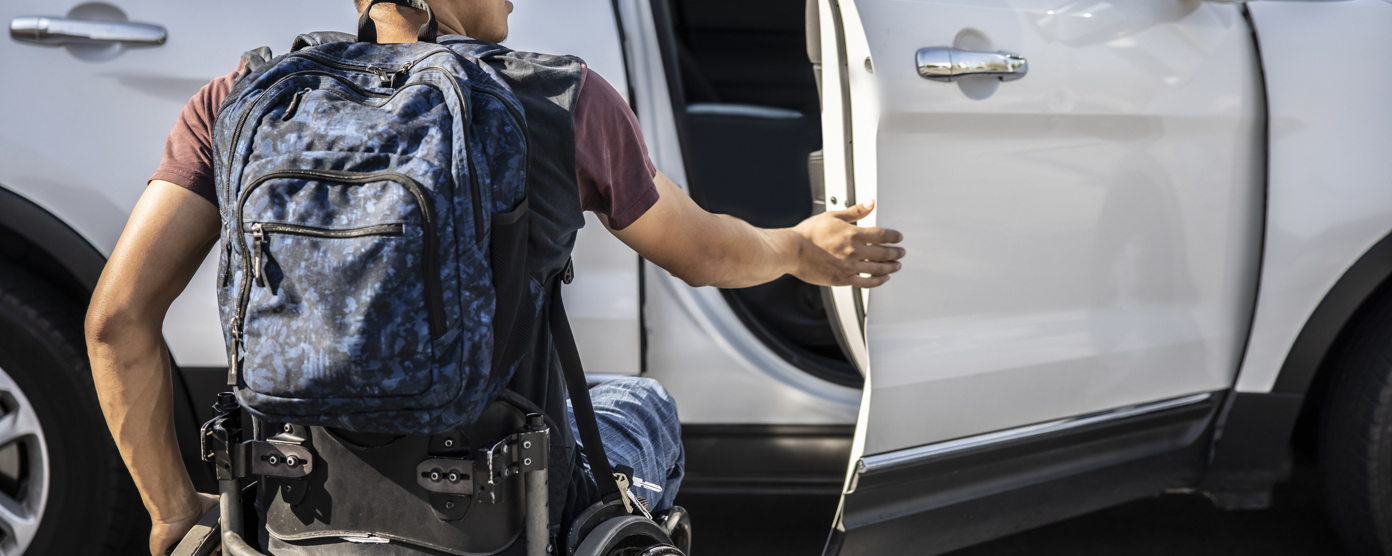 Wheelchair user with a backpack opening a car door, illustrating accessible travel and independence