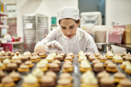 Baker in their 30s decorating vegan cupcakes in a commercial kitchen for catering.