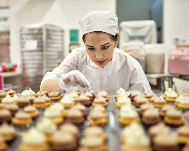 Baker in their 30s decorating vegan cupcakes in a commercial kitchen for catering.