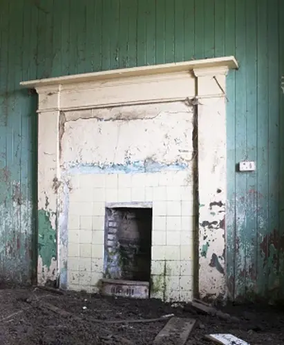 An old, damaged place with cracked tiles and peeling paint on the wall inside an abandoned room.