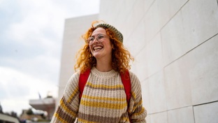 A lady with bright red hair and a jumper walks along the street smiling