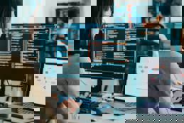 A group of Asian male and female freelancers work on AI, coding, and design projects on desktop computers.