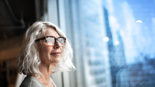 A poised businesswoman looks out a window, observing the city skyline, symbolizing her aspirations and confidence.