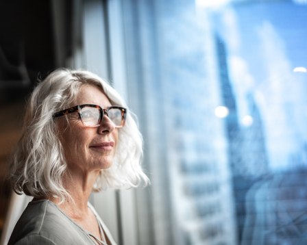A poised businesswoman looks out a window, observing the city skyline, symbolizing her aspirations and confidence.