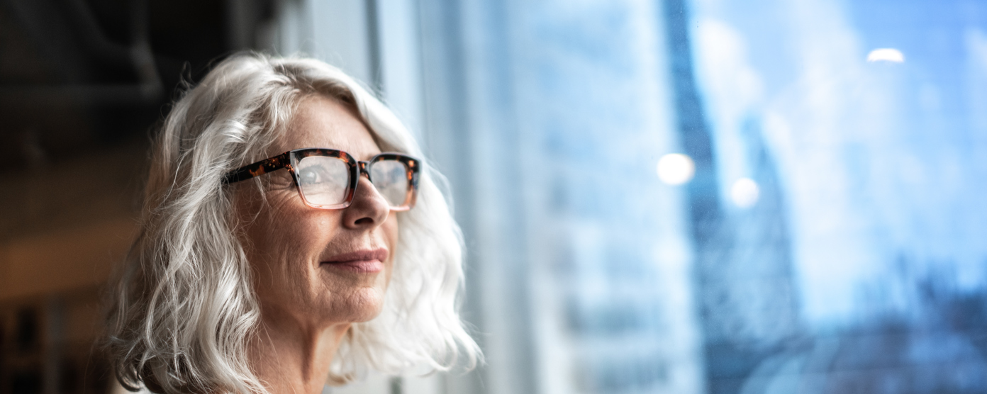 A poised businesswoman looks out a window, observing the city skyline, symbolizing her aspirations and confidence.