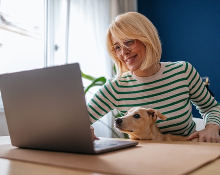 A lady sits working with her dog on her lap