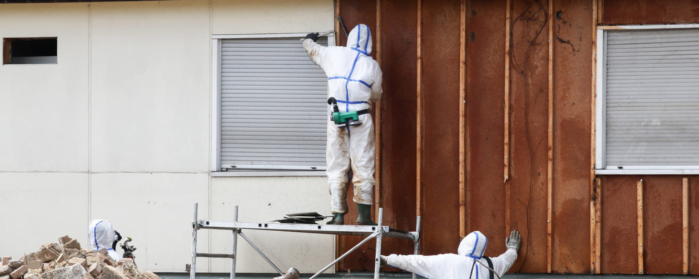 Professionals in protective suits remove asbestos on a wall