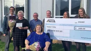 Group of award winners holding a giant cheque and flowers outside a park home after winning Park of the Year 2019