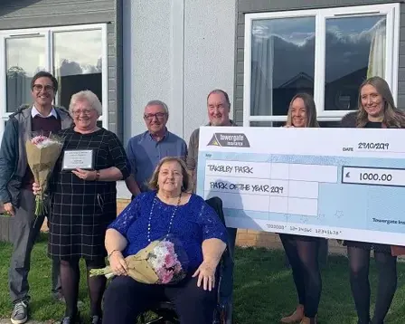 Group of award winners holding a giant cheque and flowers outside a park home after winning Park of the Year 2019