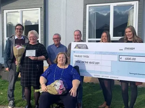 Group of award winners holding a giant cheque and flowers outside a park home after winning Park of the Year 2019