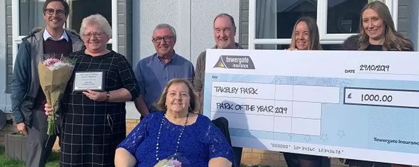 Group of award winners holding a giant cheque and flowers outside a park home after winning Park of the Year 2019