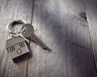 A close up of a silver house shaped keychain with a key placed on a wooden surface.