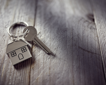 A close up of a silver house shaped keychain with a key placed on a wooden surface.