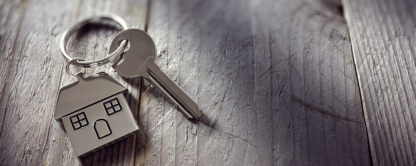 A close up of a silver house shaped keychain with a key placed on a wooden surface.