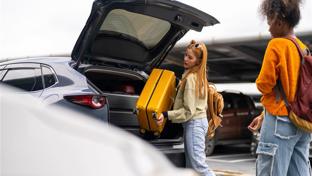 two young women loading luggage into the back of a car in a car park