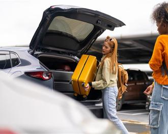 two young women loading luggage into the back of a car in a car park