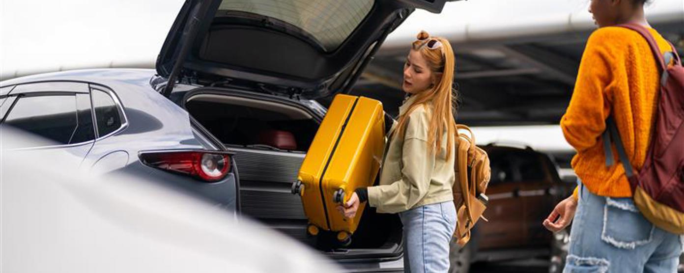 two young women loading luggage into the back of a car in a car park