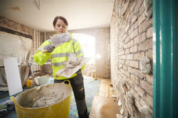 Female plasterer applying drywall adhesive