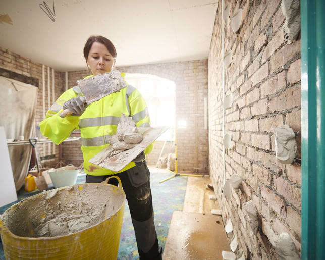 Female plasterer applying drywall adhesive