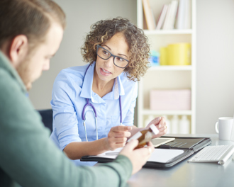 Female physician with stethoscope explains a prescription bottle to a patient during an office consultation