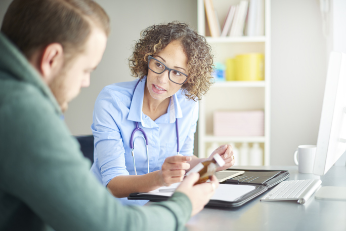 Female physician with stethoscope explains a prescription bottle to a patient during an office consultation