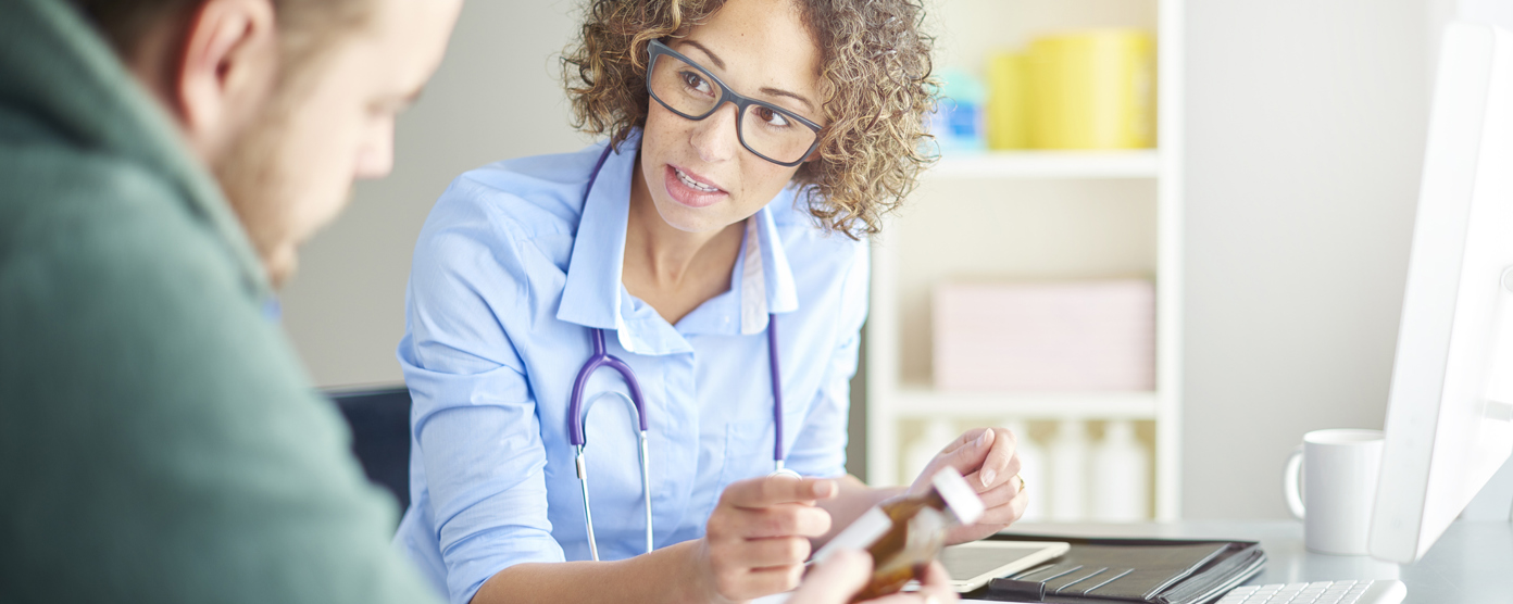Female physician with stethoscope explains a prescription bottle to a patient during an office consultation