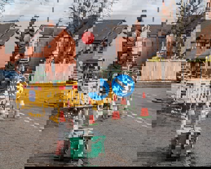 Temporary traffic lights, road signs, and cones, with construction barriers in the background.