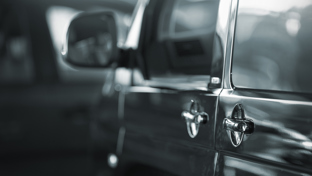 Close-up of a car’s exterior door handle with reflections and side mirror in soft focus, parked indoors