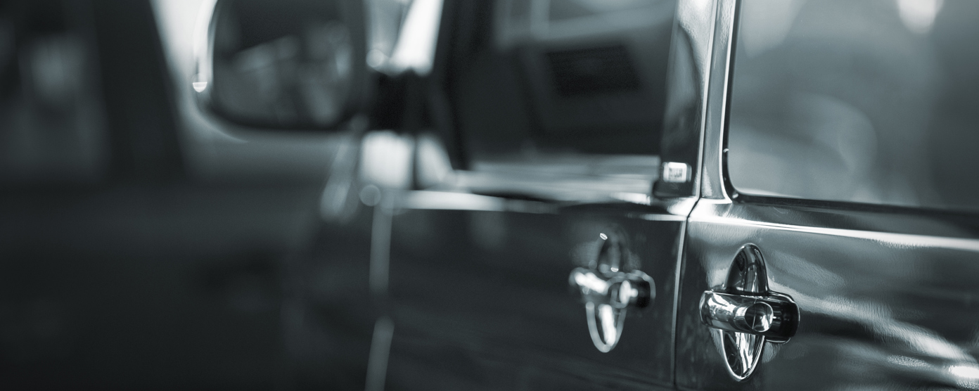 Close-up of a car’s exterior door handle with reflections and side mirror in soft focus, parked indoors