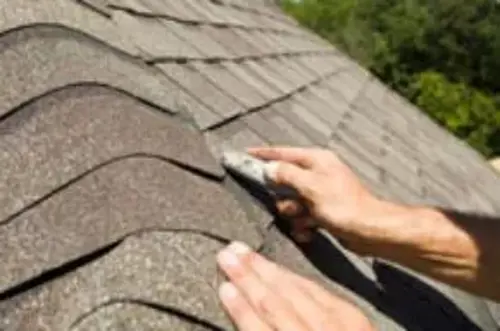 Hands installing or repairing asphalt roof shingles.