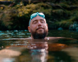 Man with eyes closed with goggles on his head swimming in nature