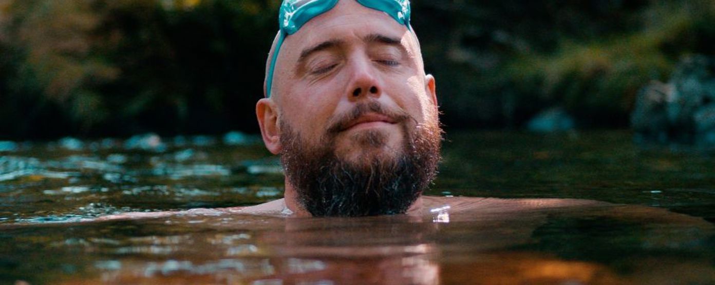 Man with eyes closed with goggles on his head swimming in nature