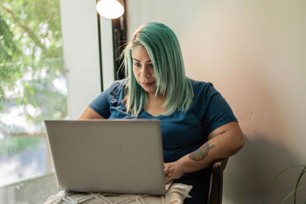 Lady with green hair and tattoos working on her laptop at a table