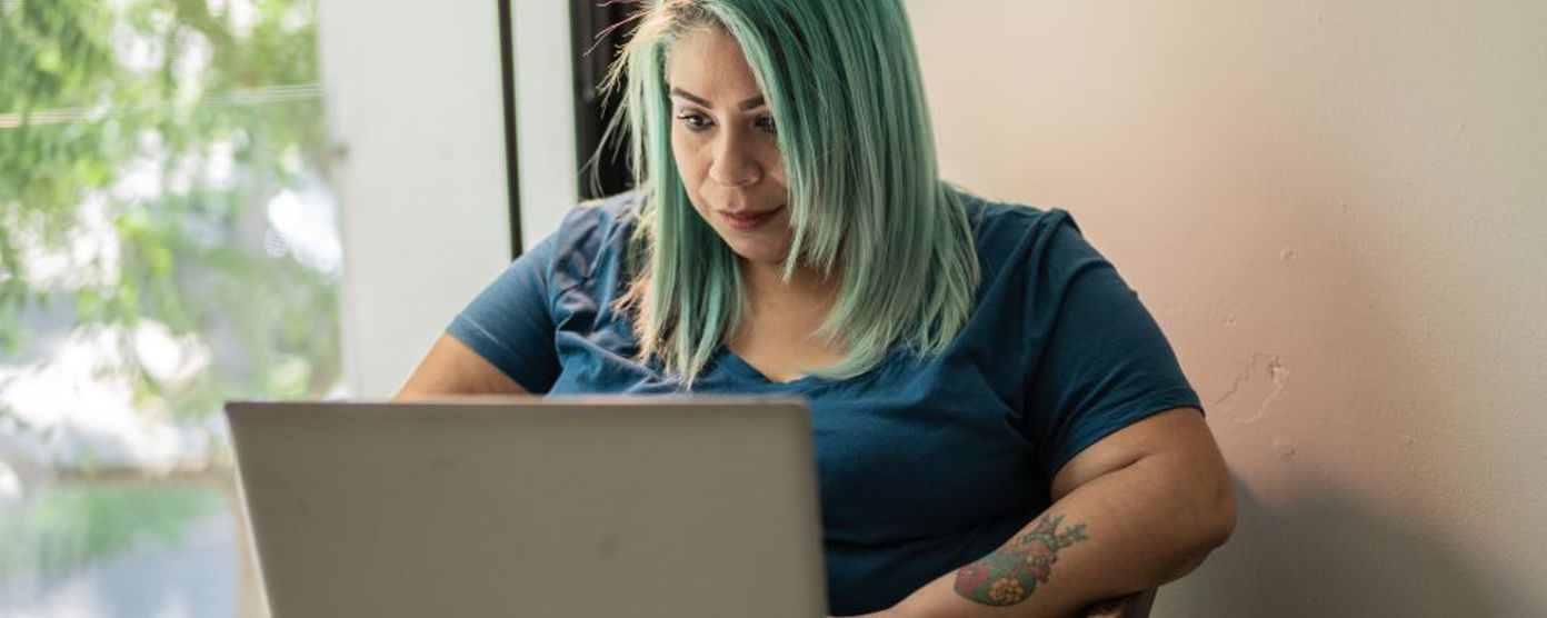 Lady with green hair and tattoos working on her laptop at a table